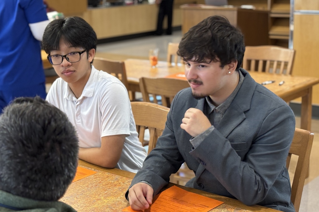 Three young men sit at a table, engaged in conversation.