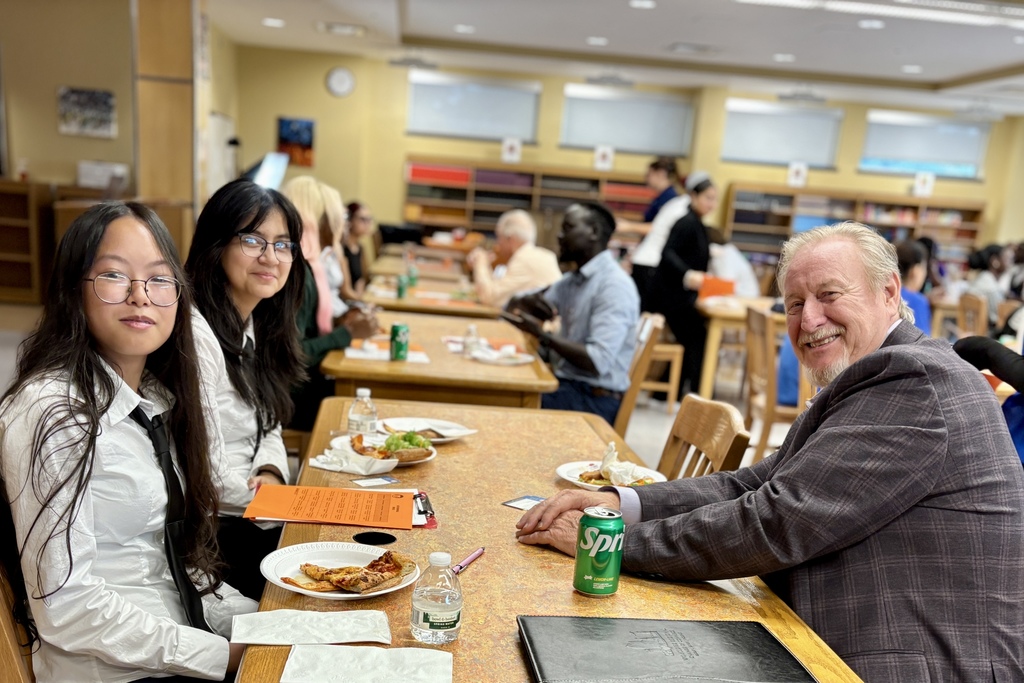 People sit at tables in a room, some smiling at the camera.