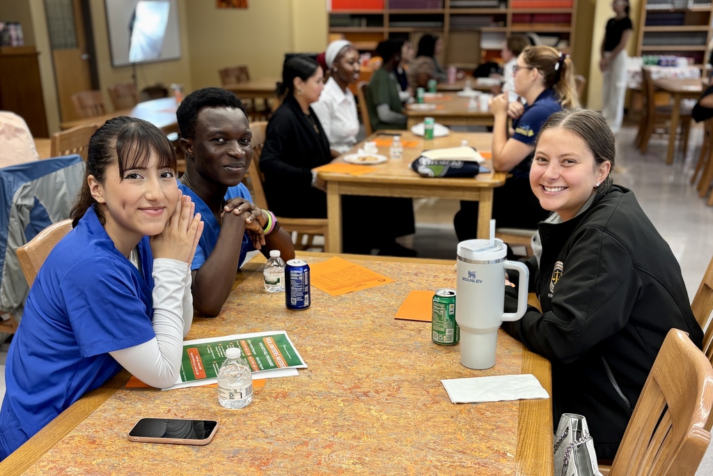 A group of people sit at tables, smiling and looking at the camera.