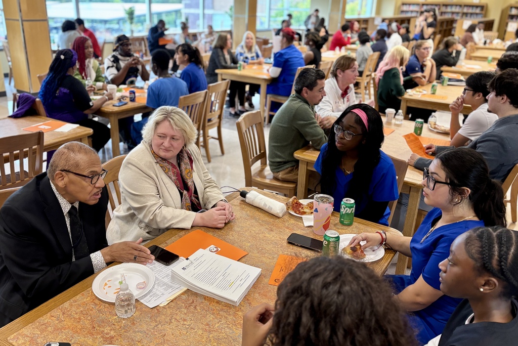 A diverse group of people sit at tables, engaged in conversation and enjoying food.