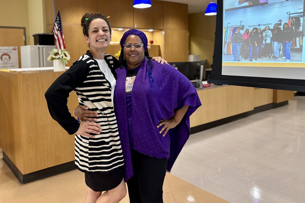 Two women smile and pose together, one with a striped jacket and the other in purple.