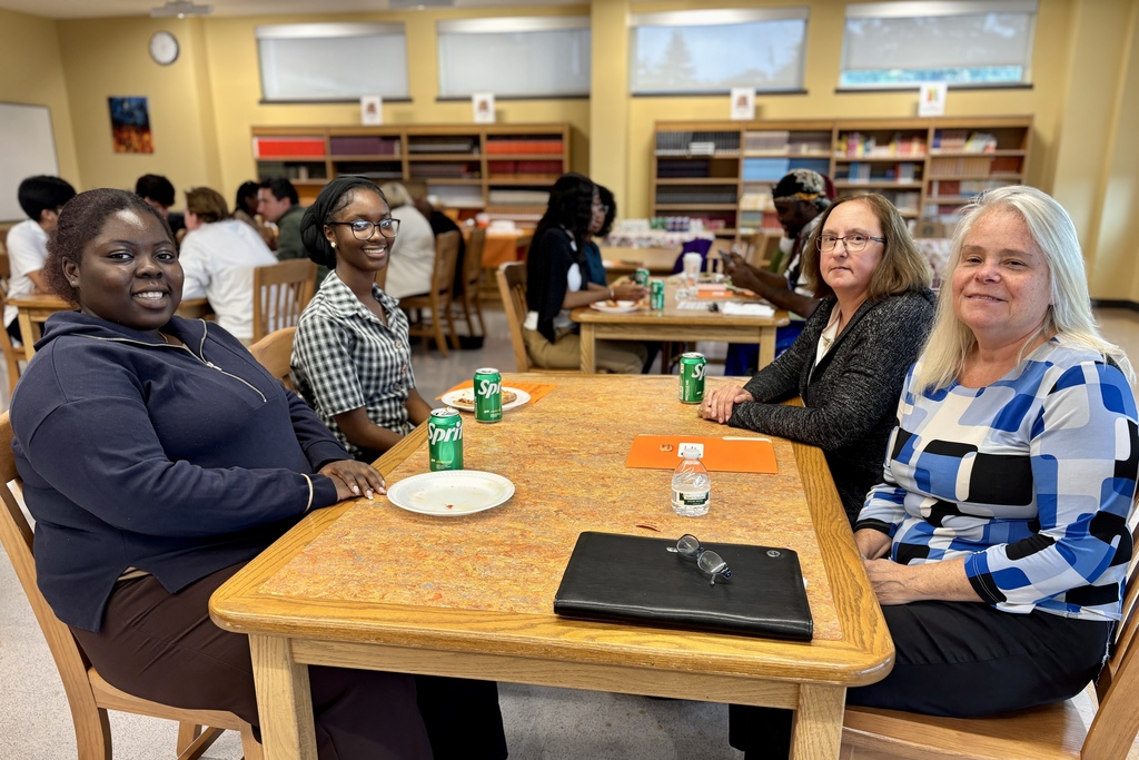 A group of people sit around a table in a library, smiling and looking at the camera.