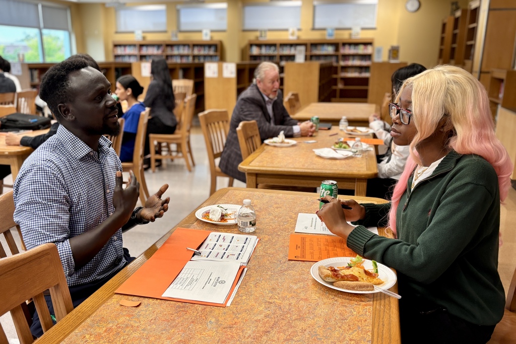 A group of people sit at tables, smiling and looking at the camera.