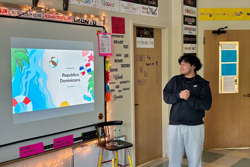 A student stands in a classroom, presenting a slideshow about the Dominican Republic.