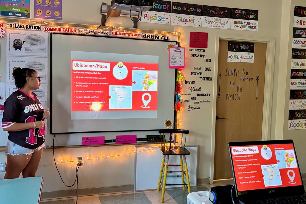 A student presents a map on a projector screen in a classroom setting.