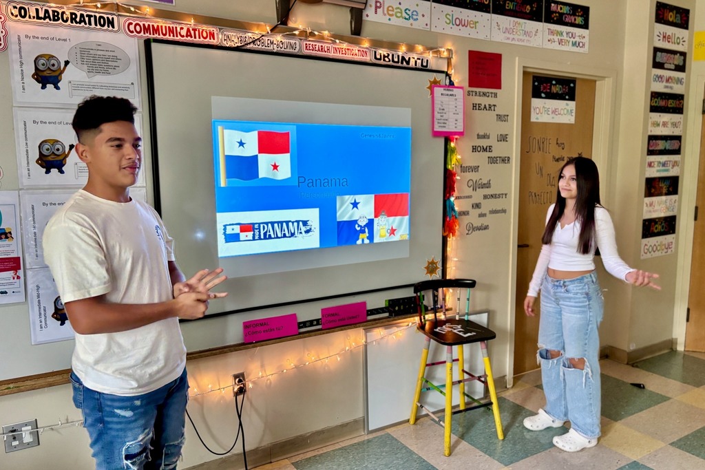Two students present in a classroom, with a screen displaying the flag of Panama.