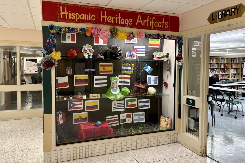 A display case showcases Hispanic Heritage artifacts, including flags and cultural items.