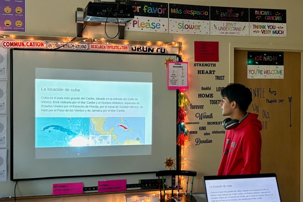 A student stands in a classroom, looking at a presentation about Cuba.