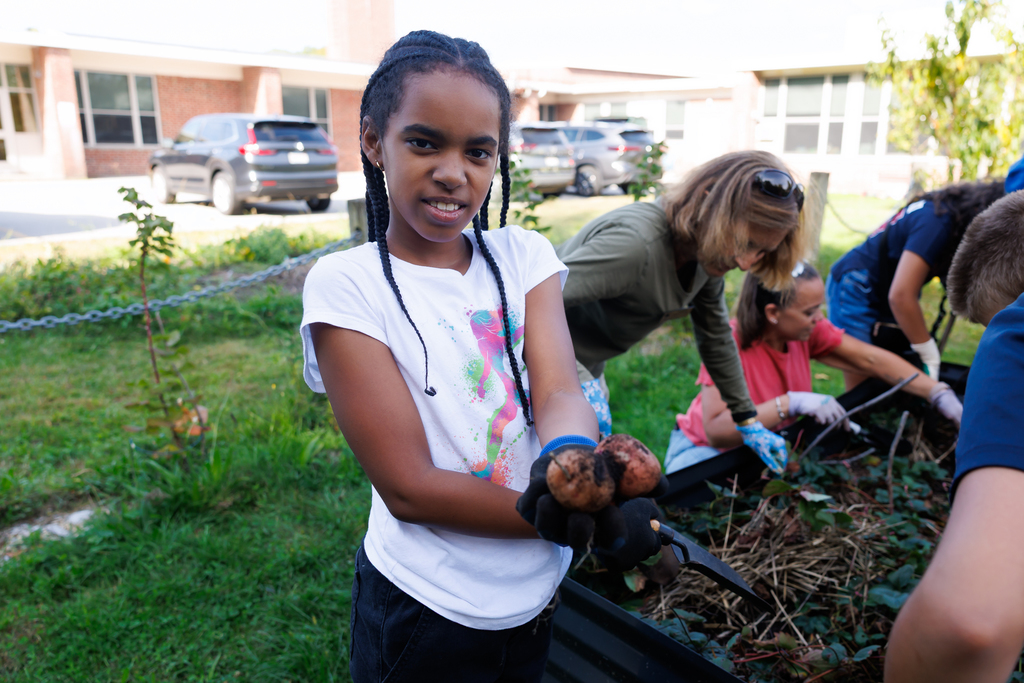 A student holds out their freshly harvested potatoes.