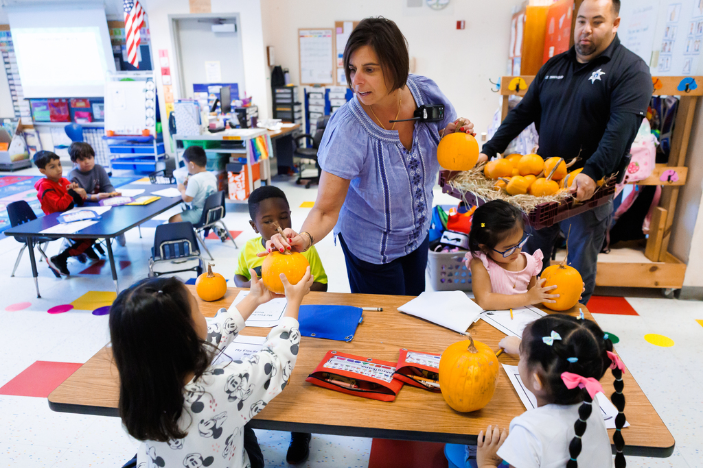 A teacher gives kindergarten students a pumpkin.