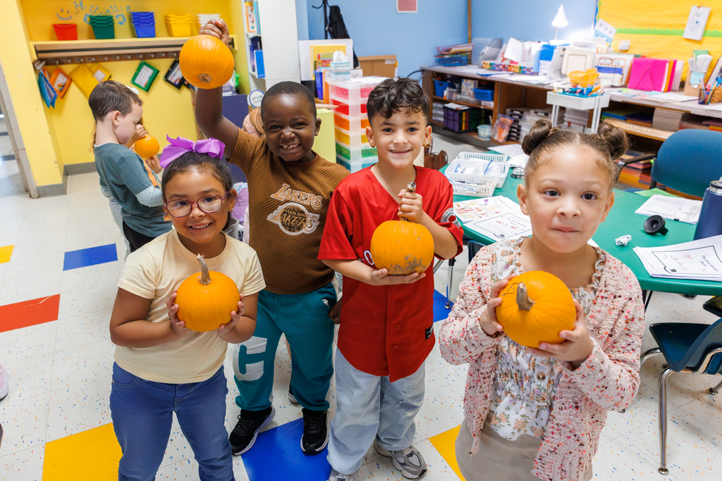 Four students hold up their pumpkins.