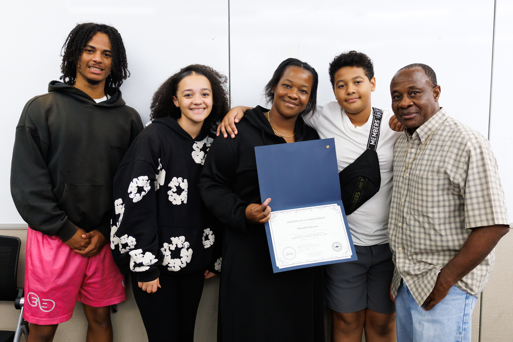 A family of five stand together for a photo, one of them is holding a certificate of completion.