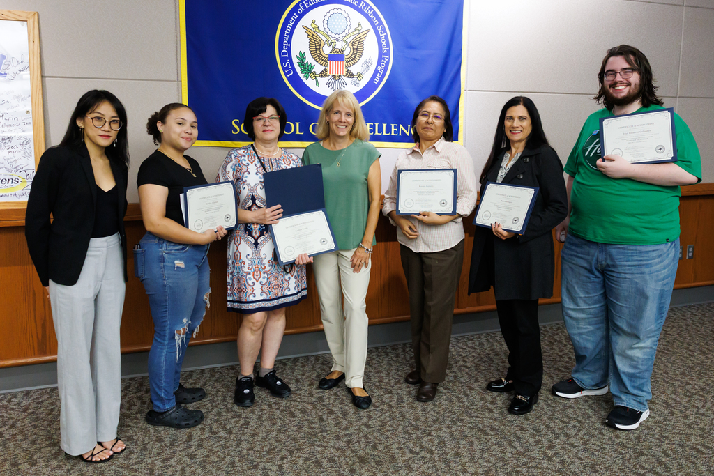 A teacher and adult night life students hold up a certificate of completion.