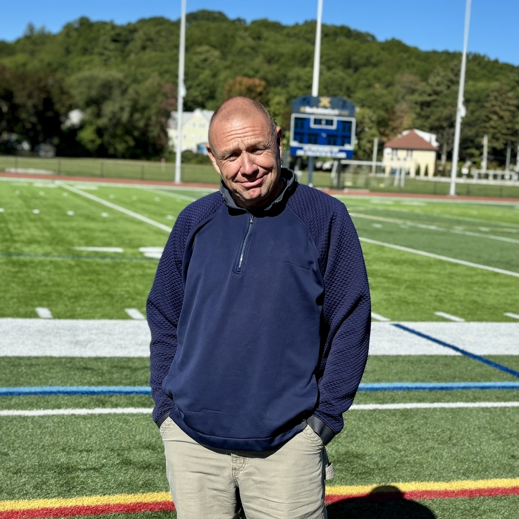 A man stands on a football field, smiling at the camera.