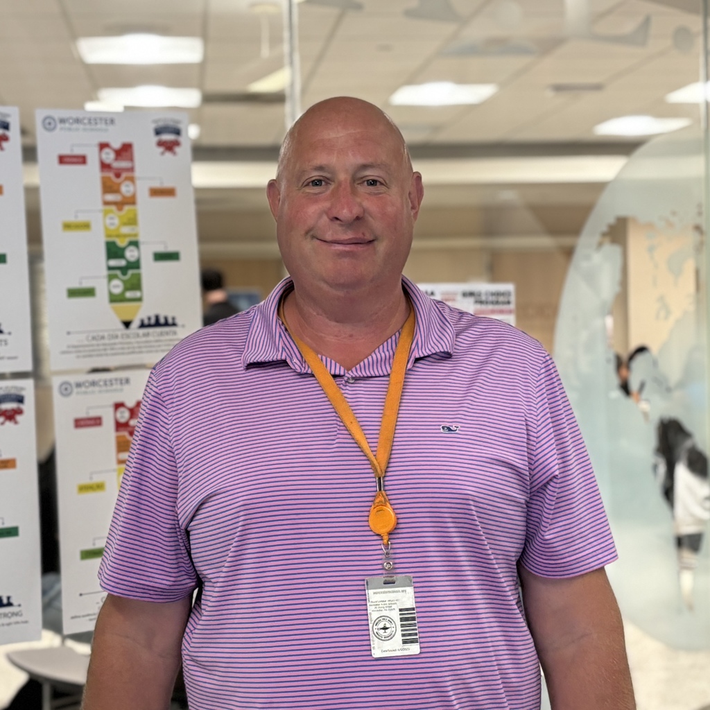 A man in a pink striped shirt smiles at the camera, wearing a lanyard.