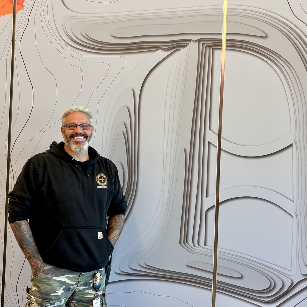 A smiling man stands in front of a large, abstract wall art piece.