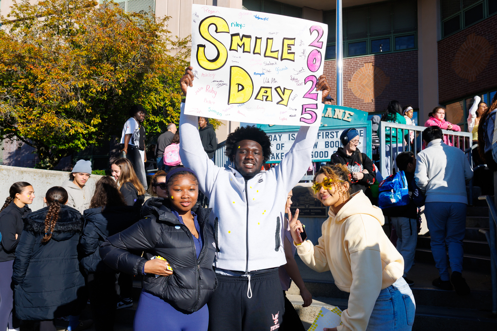 Three students smile for a photo, one of them is holding a sign that says "Smile Day" 2025.