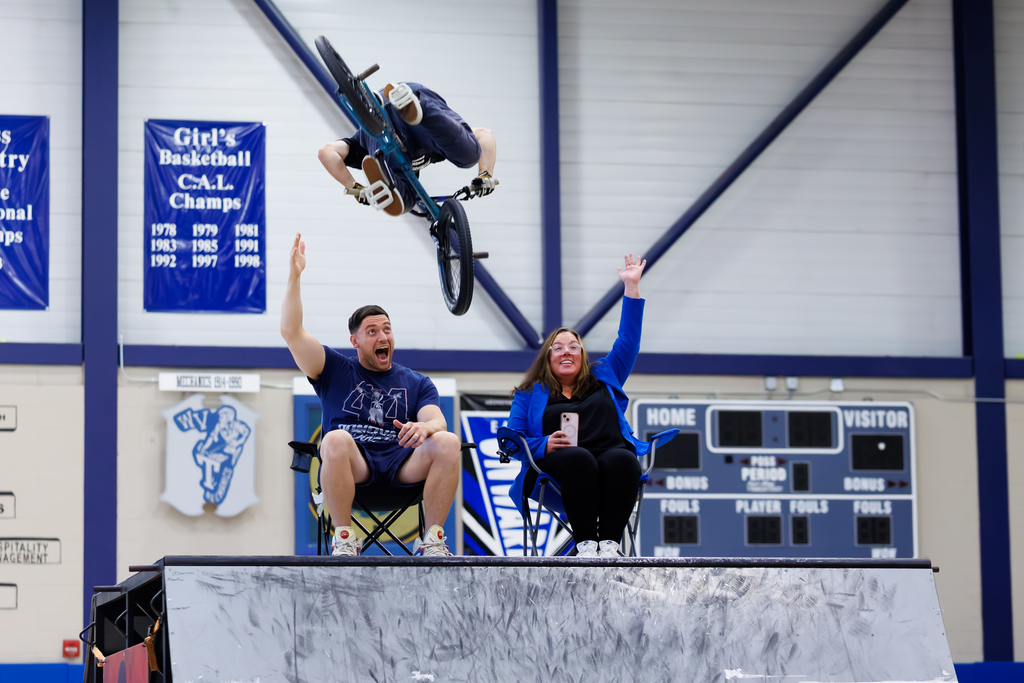 A BMX biker jumps over two staff members from Worcester Tech.