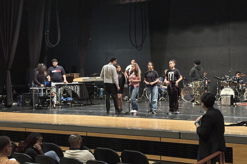 A group of people stand on a stage, possibly rehearsing or performing.