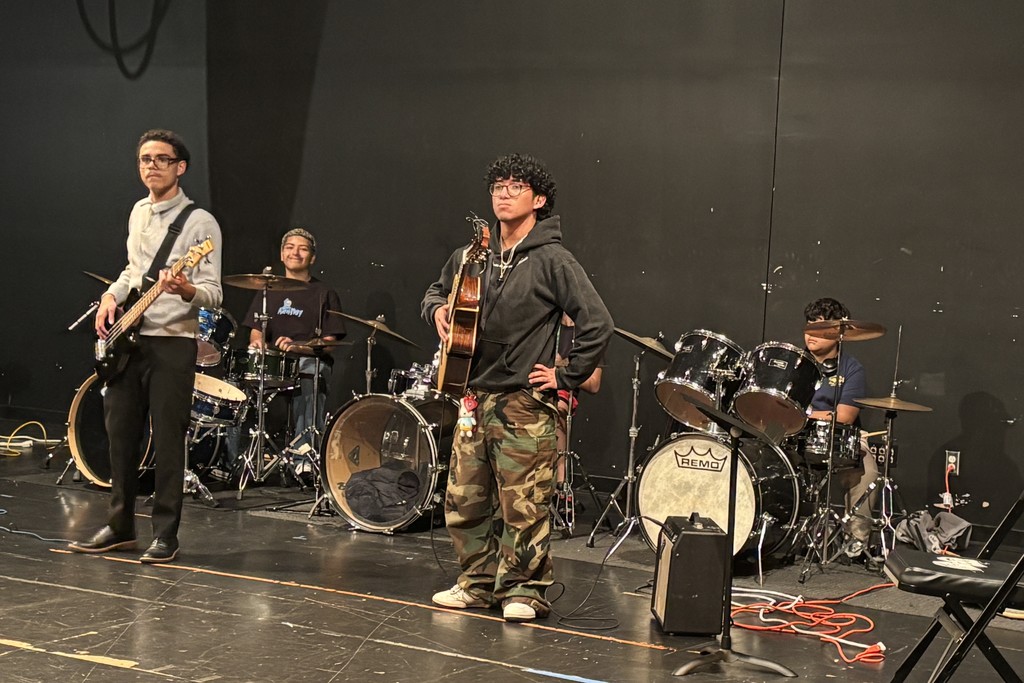 A band of young musicians prepares to perform on a stage, instruments ready.