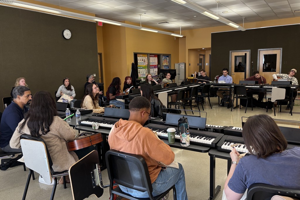 A music class is in session, with students seated at keyboards and guitars.