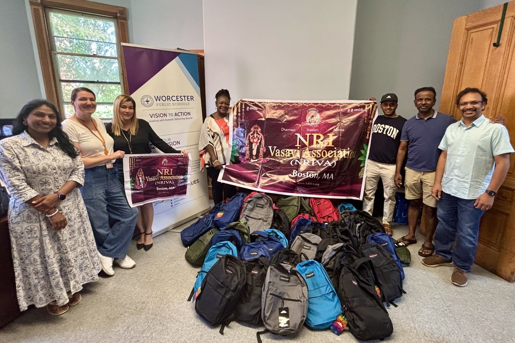 A group of people pose with backpacks and a banner for the NRI Vasavi Association.