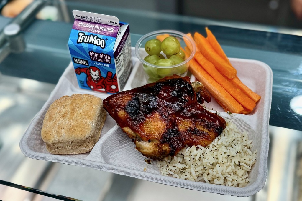 A school lunch tray with chicken, rice, vegetables, a biscuit, and chocolate milk.