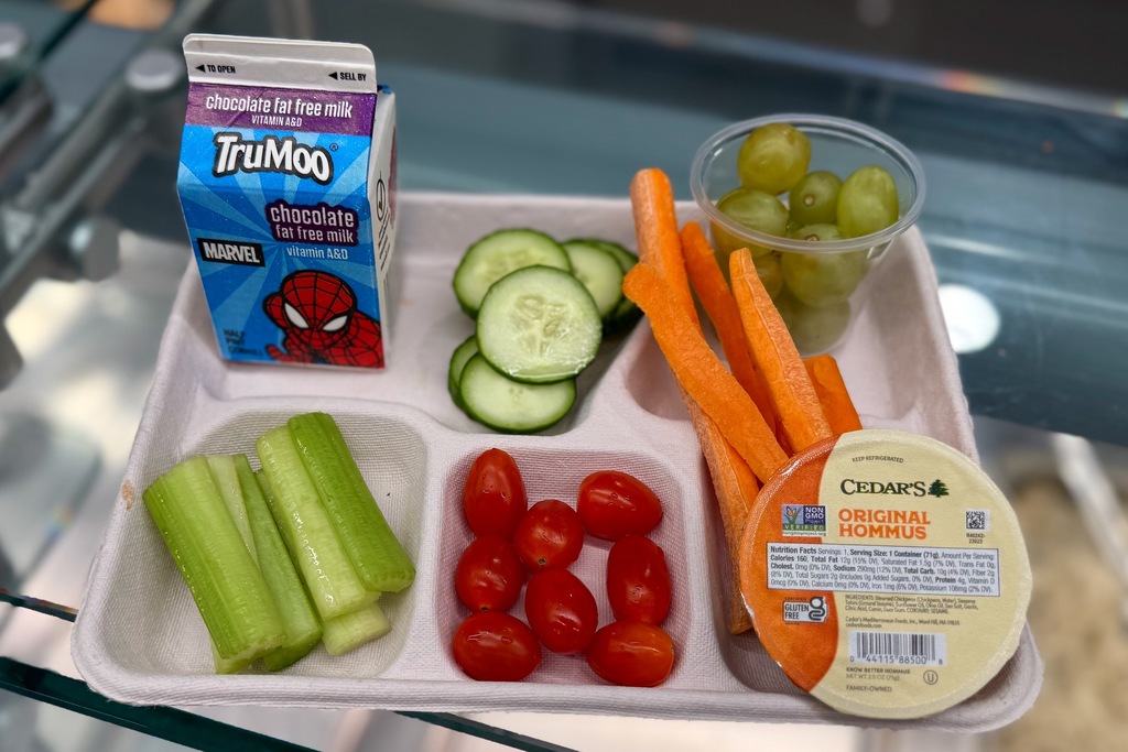 A tray with a balanced lunch: vegetables, hummus, grapes, and chocolate milk.