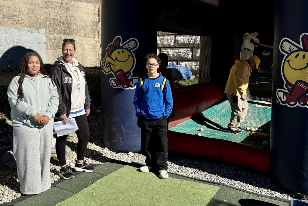 Three people stand near a baseball-themed inflatable, with a person inside.