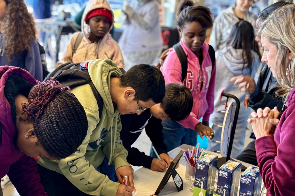A group of people gather around a table, some writing and looking at a display.