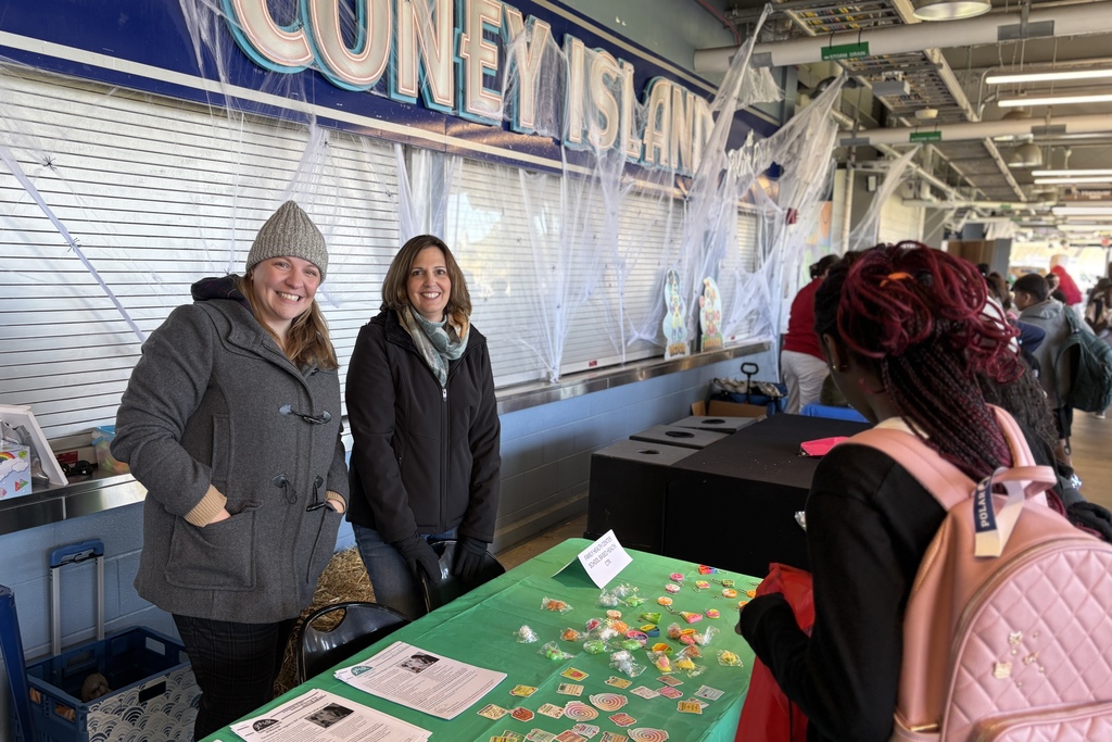 Two women smile at the camera near a table with treats and information.