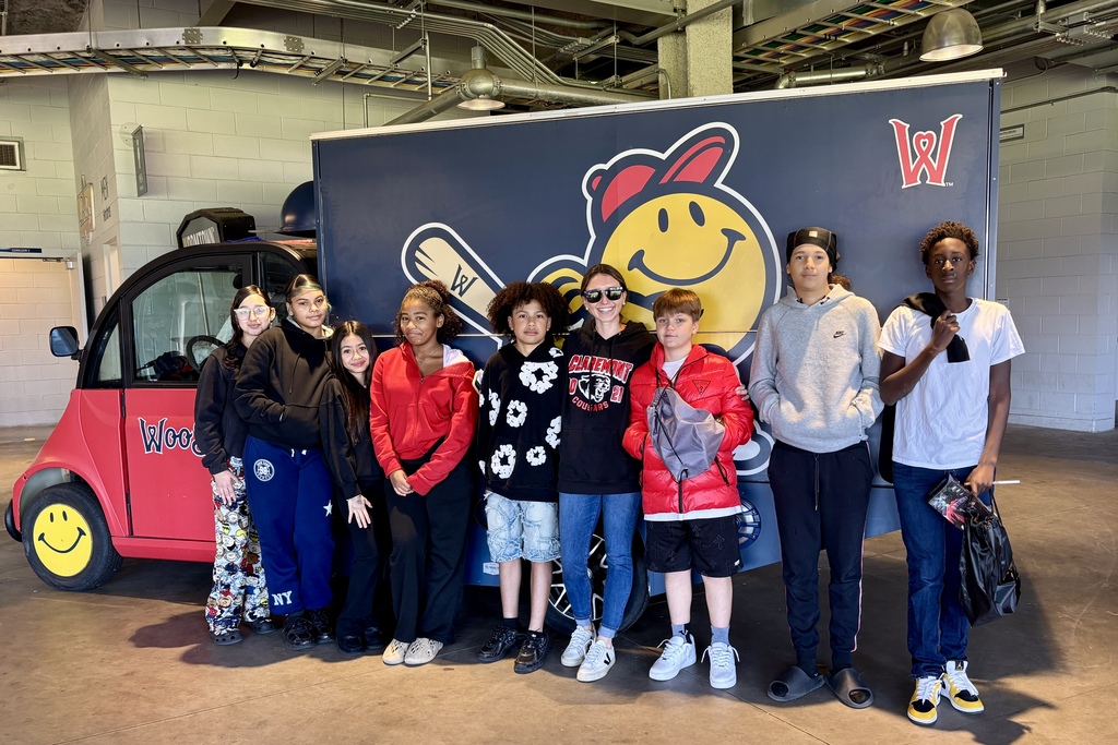 A group of diverse teens pose in front of a baseball-themed truck and a small red vehicle.