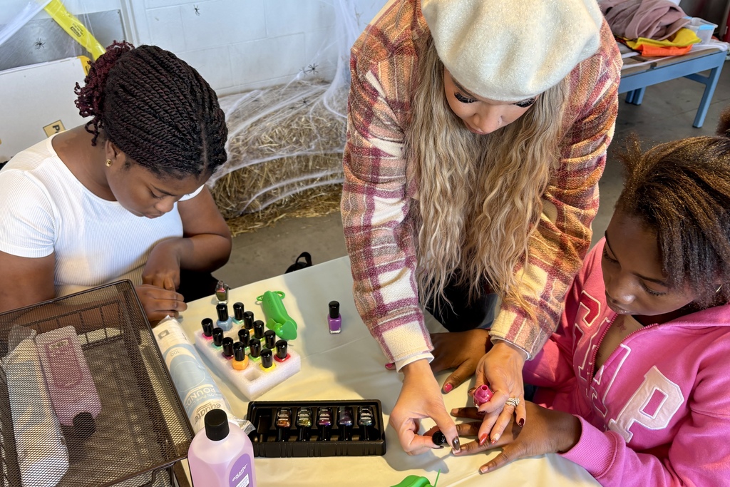 Three people are gathered around a table, doing manicures with various nail polish colors.