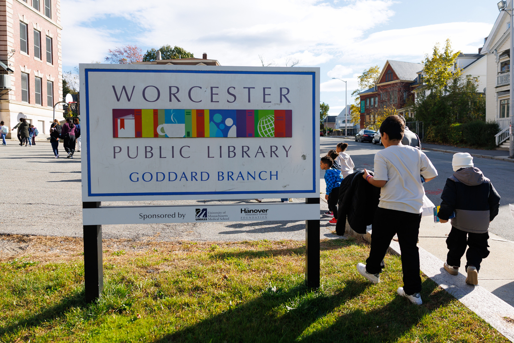 Students walk on the sidewalk past a sign that says "Worcester Public Library Goddard Branch."