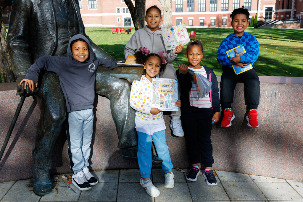 Five students sit together holding up books and smiling.