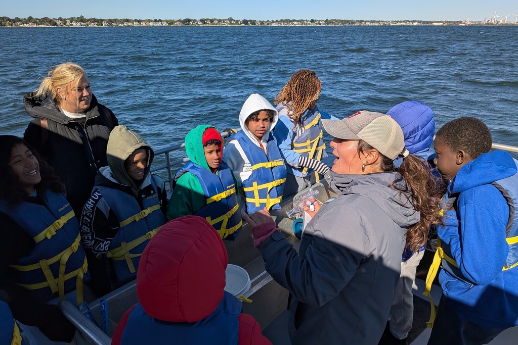 A group of people on a boat, wearing life vests, look out at the water.