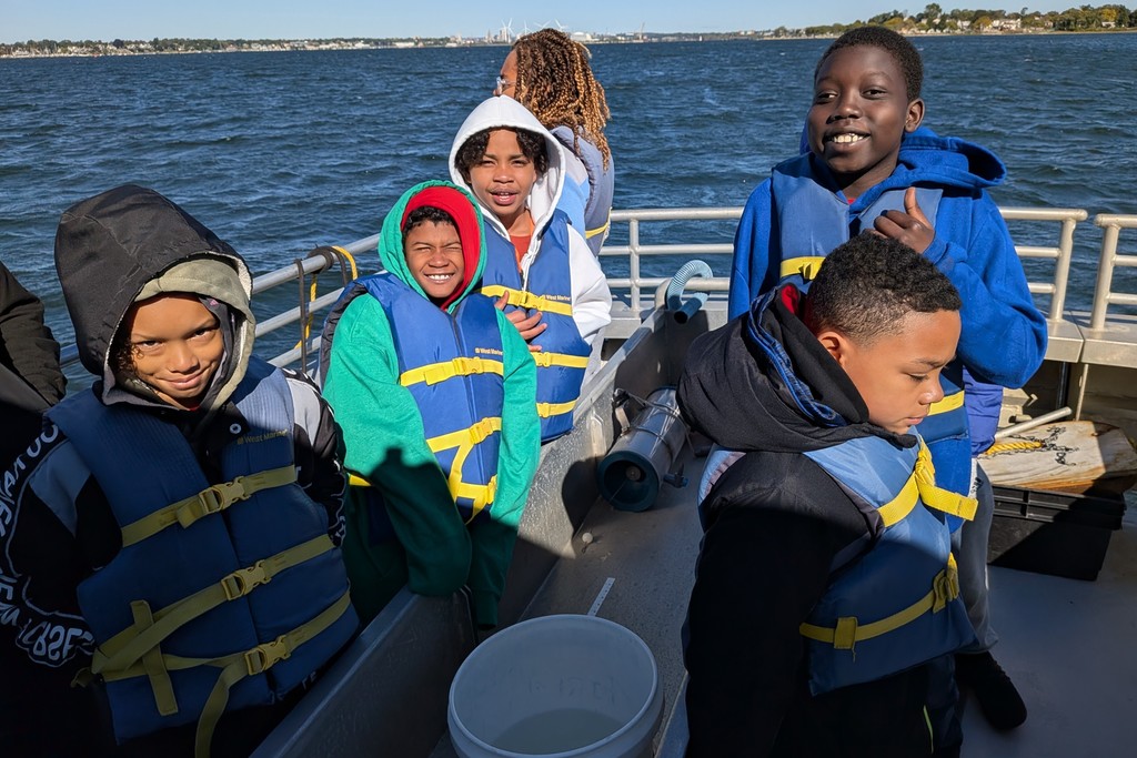 A group of children wearing life vests on a boat, smiling at the camera.