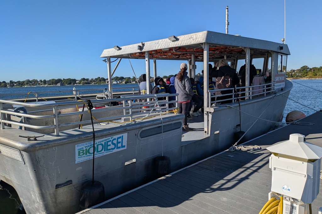 People board a boat at a dock on a sunny day, with life vests visible.