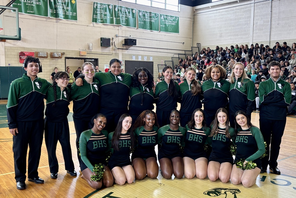 A group of students in green and black uniforms pose for a photo in a gymnasium.