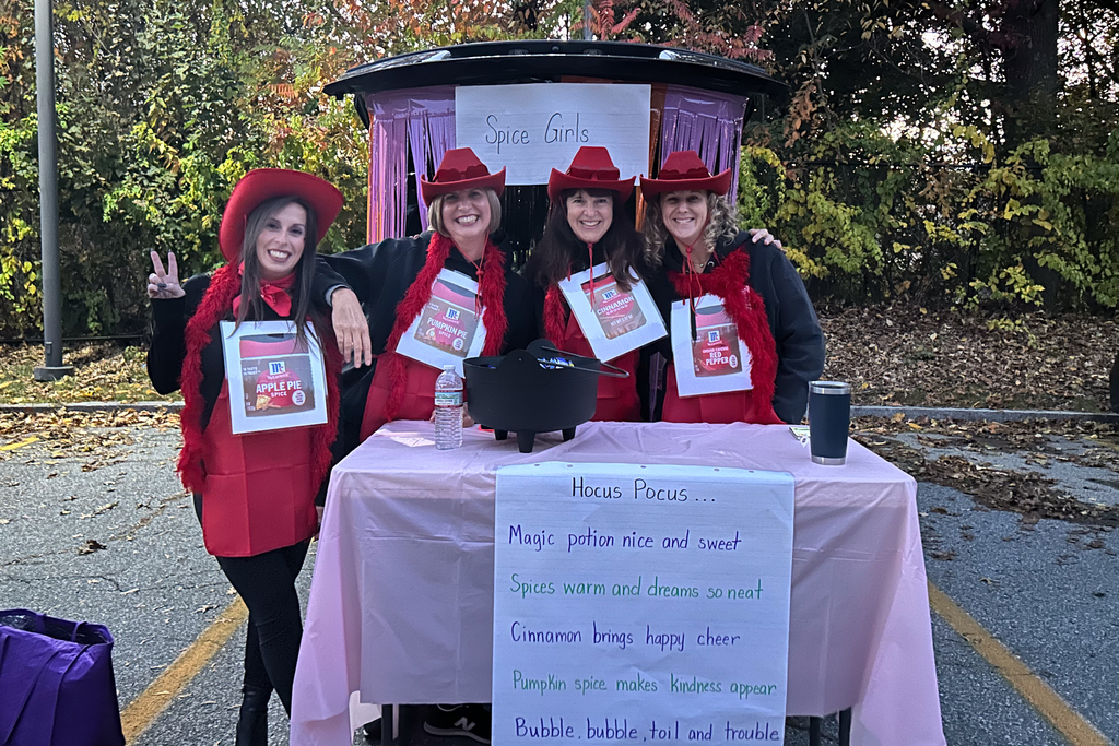 A table of adults dressed as "Spice Girls" each wearing a sign of a cooking spice. 