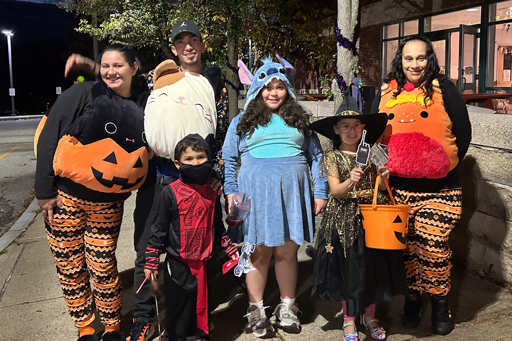 A family of six stand together dressed in costumes during a Trunk or Treat.