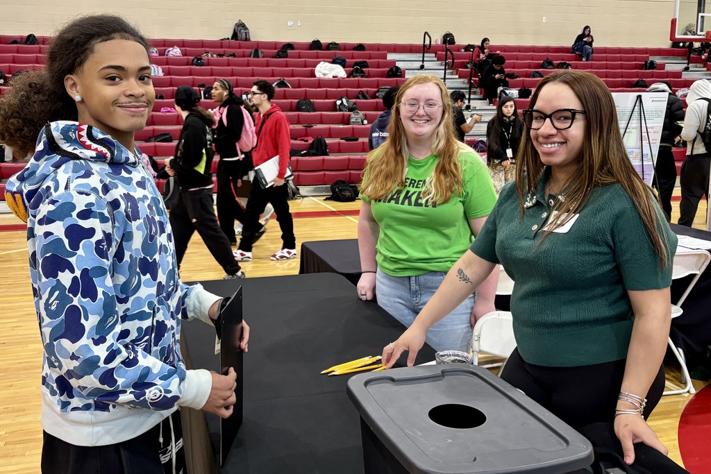 Three people stand behind a table in a gymnasium, smiling at the camera.