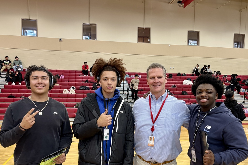 Four people pose for a photo in a gymnasium, smiling at the camera.