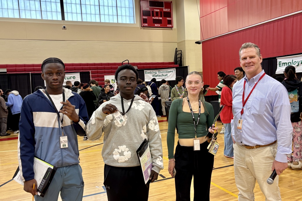 Four people stand in a gymnasium, likely at a career fair or event.