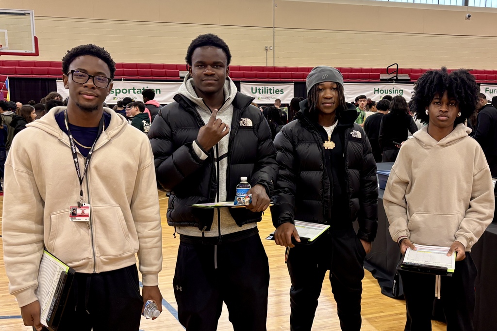 Four young men stand together in a gymnasium, holding clipboards.