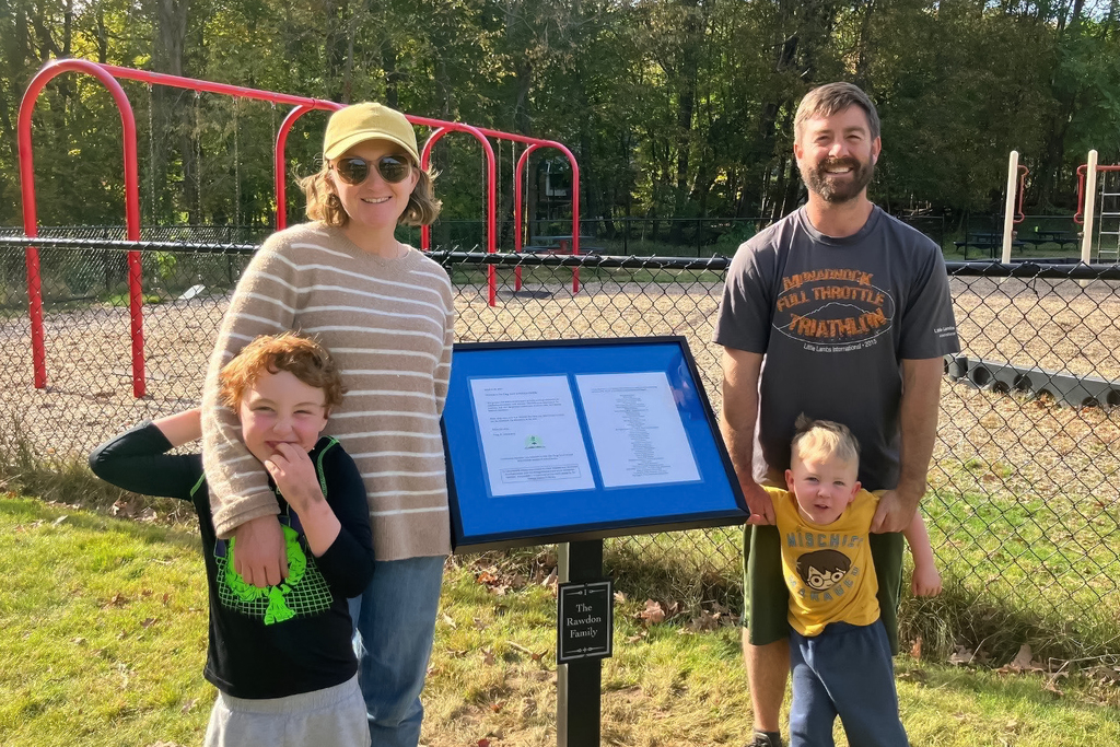 A family poses together in front of a sign at a school.