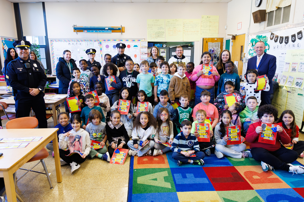 A group of children and adults pose for a photo in a colorful classroom.