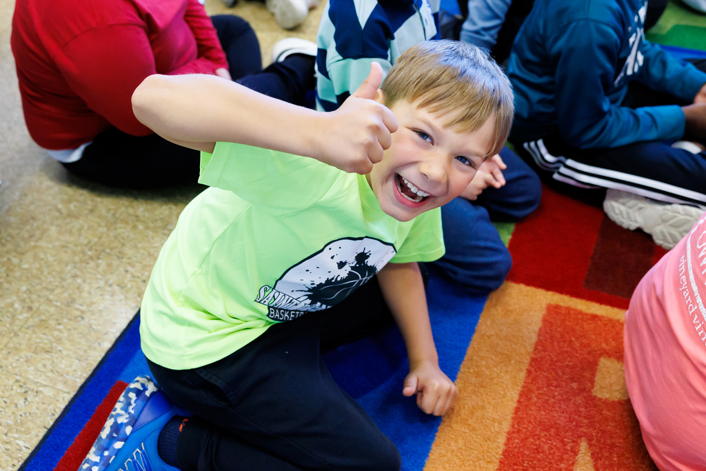 A smiling boy gives a thumbs up, looking happy and excited.