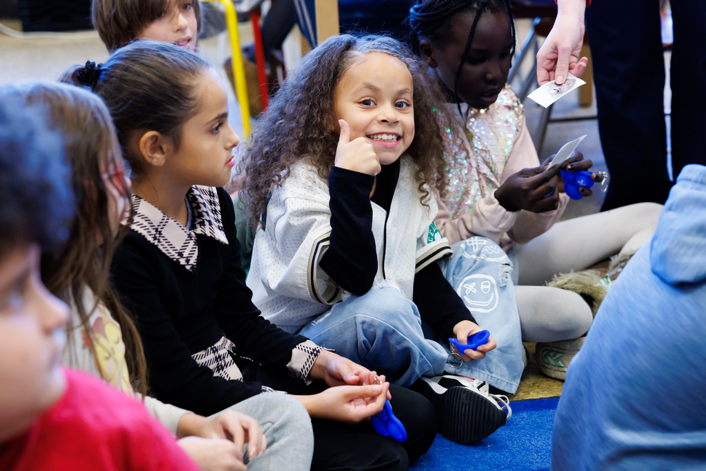 A group of children sit together, some holding blue objects.
