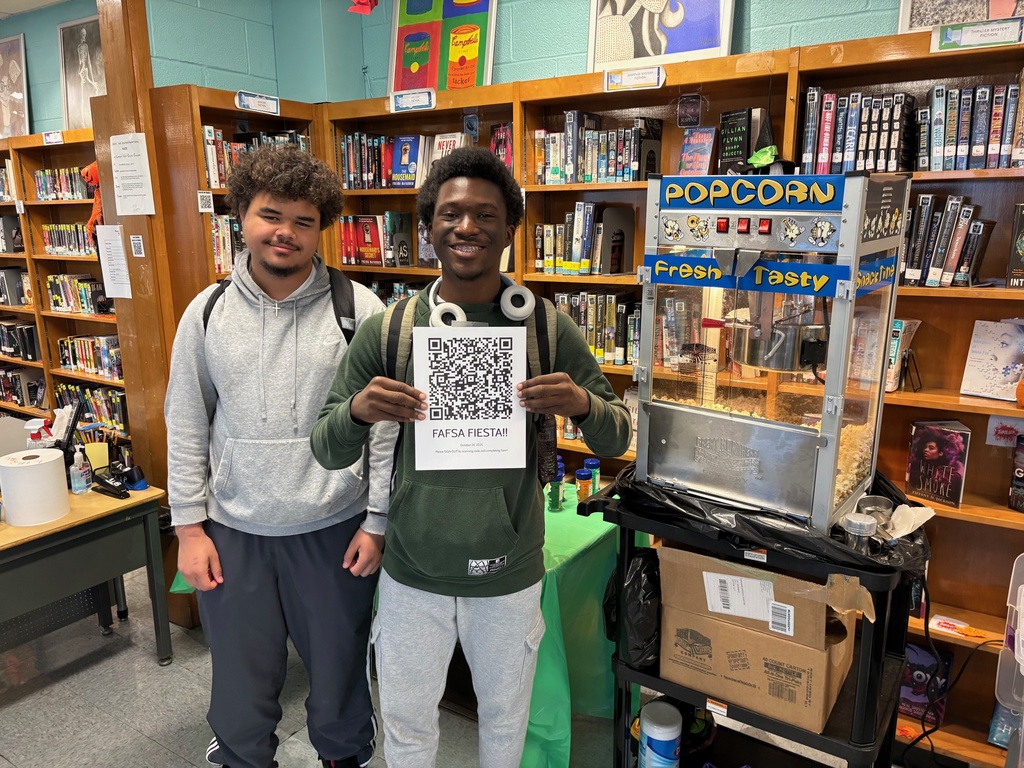 Two students smile for a photo, one of them is holding up a flyer with a QR code. 